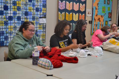 Three women seated and working on fiber arts projects