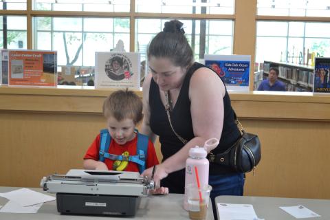 A woman and child sit at a table with a typewriter