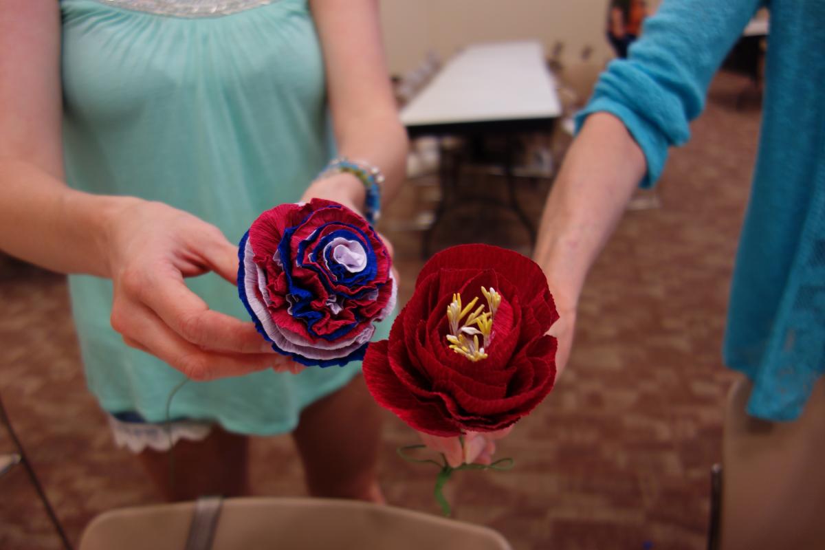 Two people holding brightly colored paper flowers