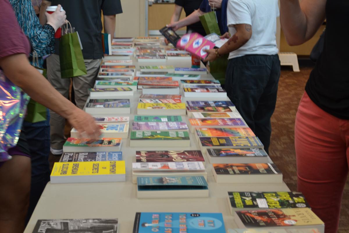 Table full of books and people gathered around perusing books