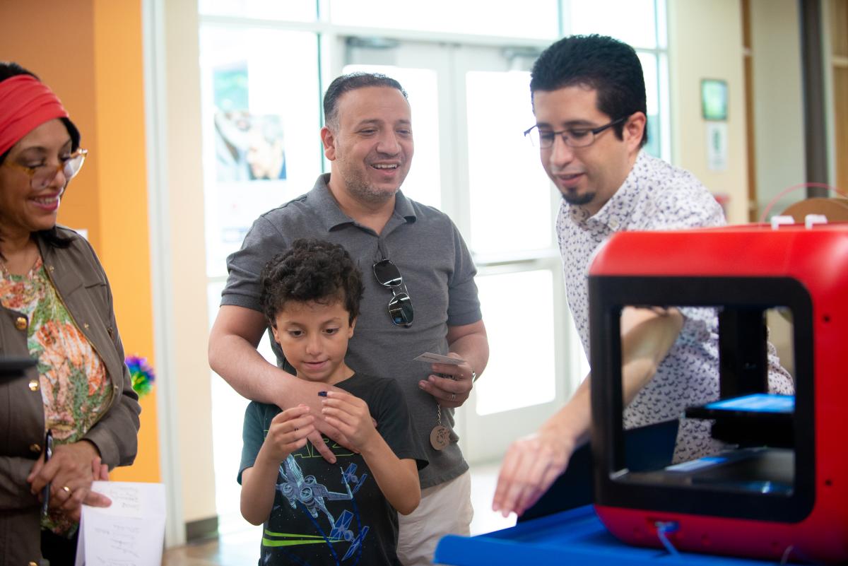 Library staff and visitors gathered around the library's 3D printer