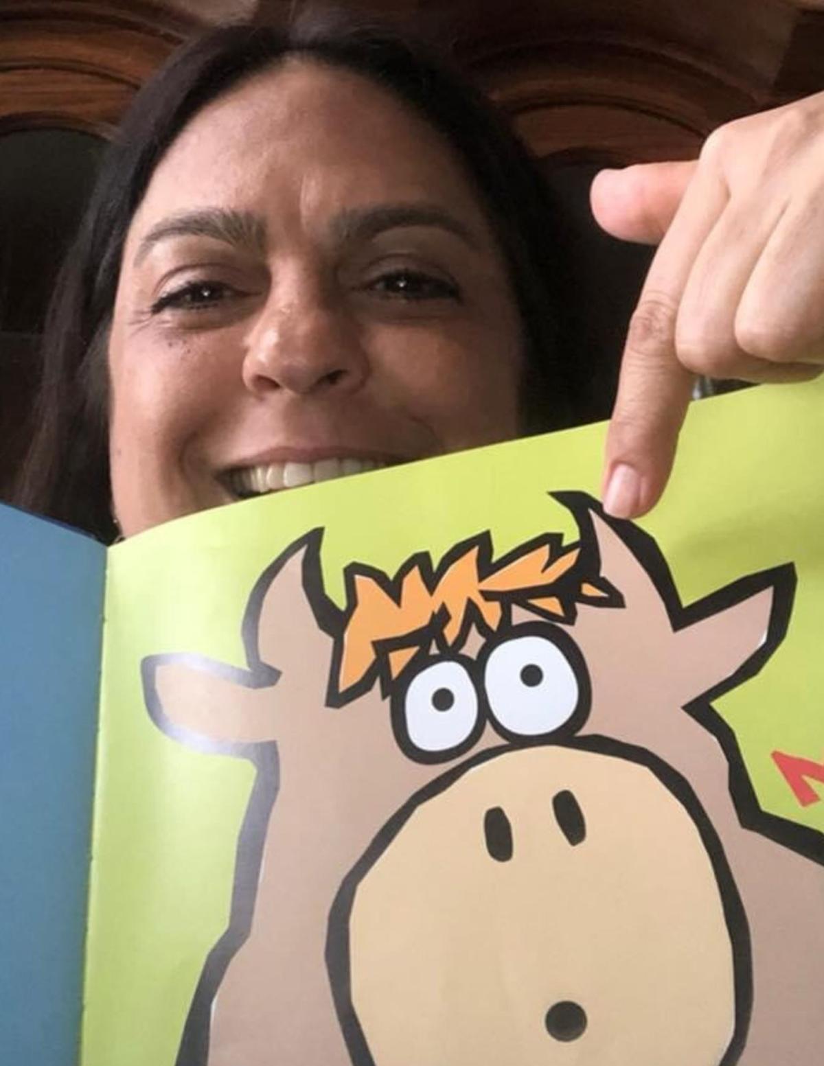 Female adult reading picture book with a cow to children